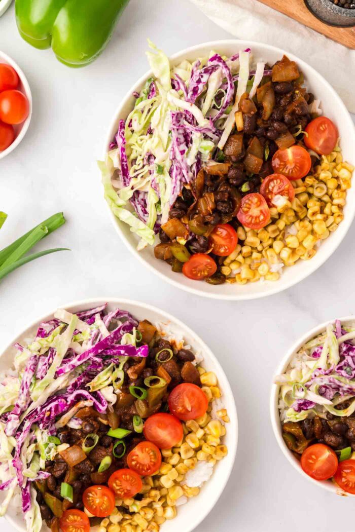 Two colourful plant-based bowls with rice, corn, tomato, cabbage slaw and BBQ black beans arranged nicely in the bowls.