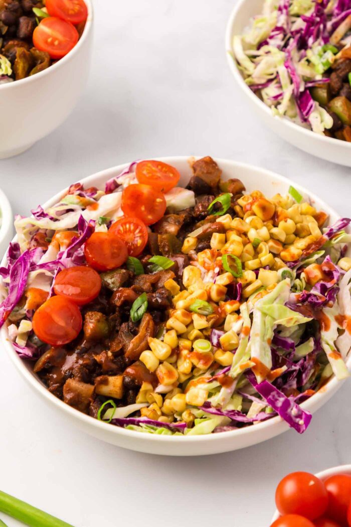 A colourful vegetable bean and rice bowl with corn, tomato and red and green cabbage slaw with BBQ sauce drizzled on top.