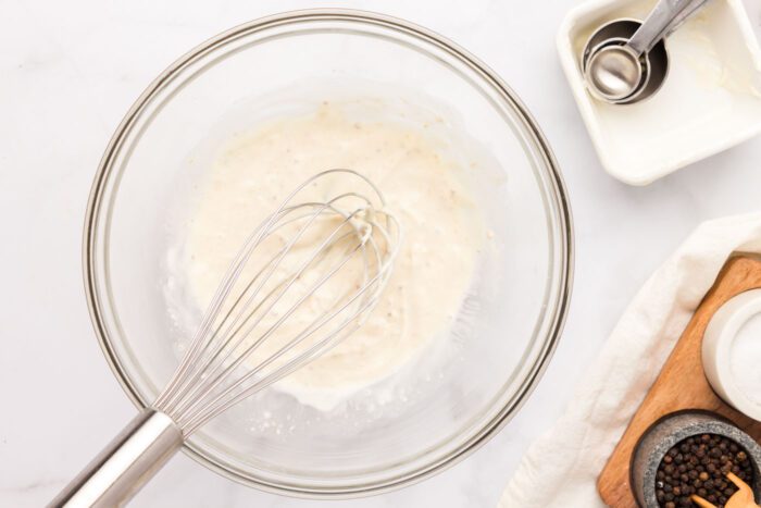 A creamy mayo-based mixture in a glass mixing bowl with a whisk in it.