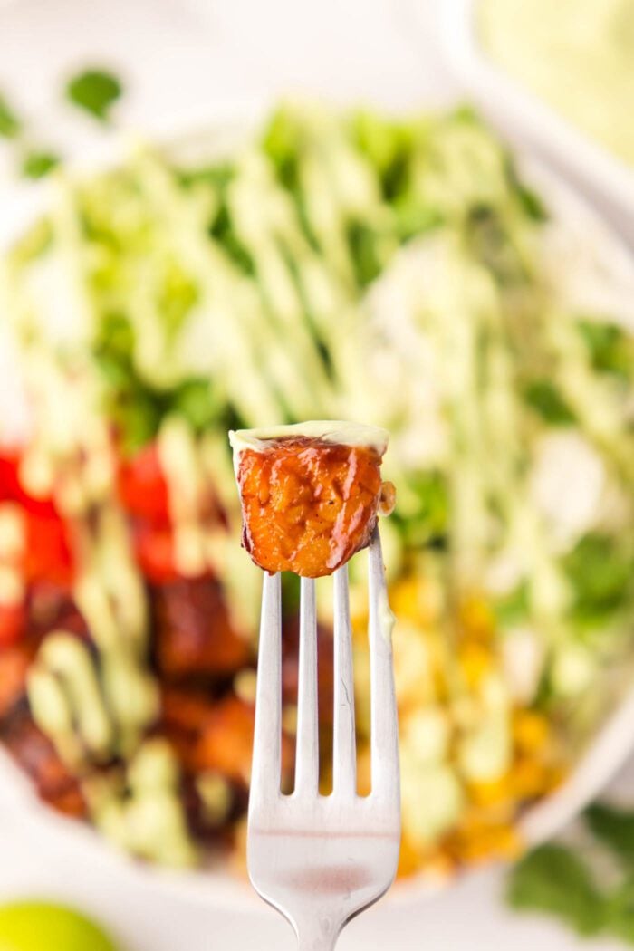 A cube of BBQ tempeh on a fork held over a salad.