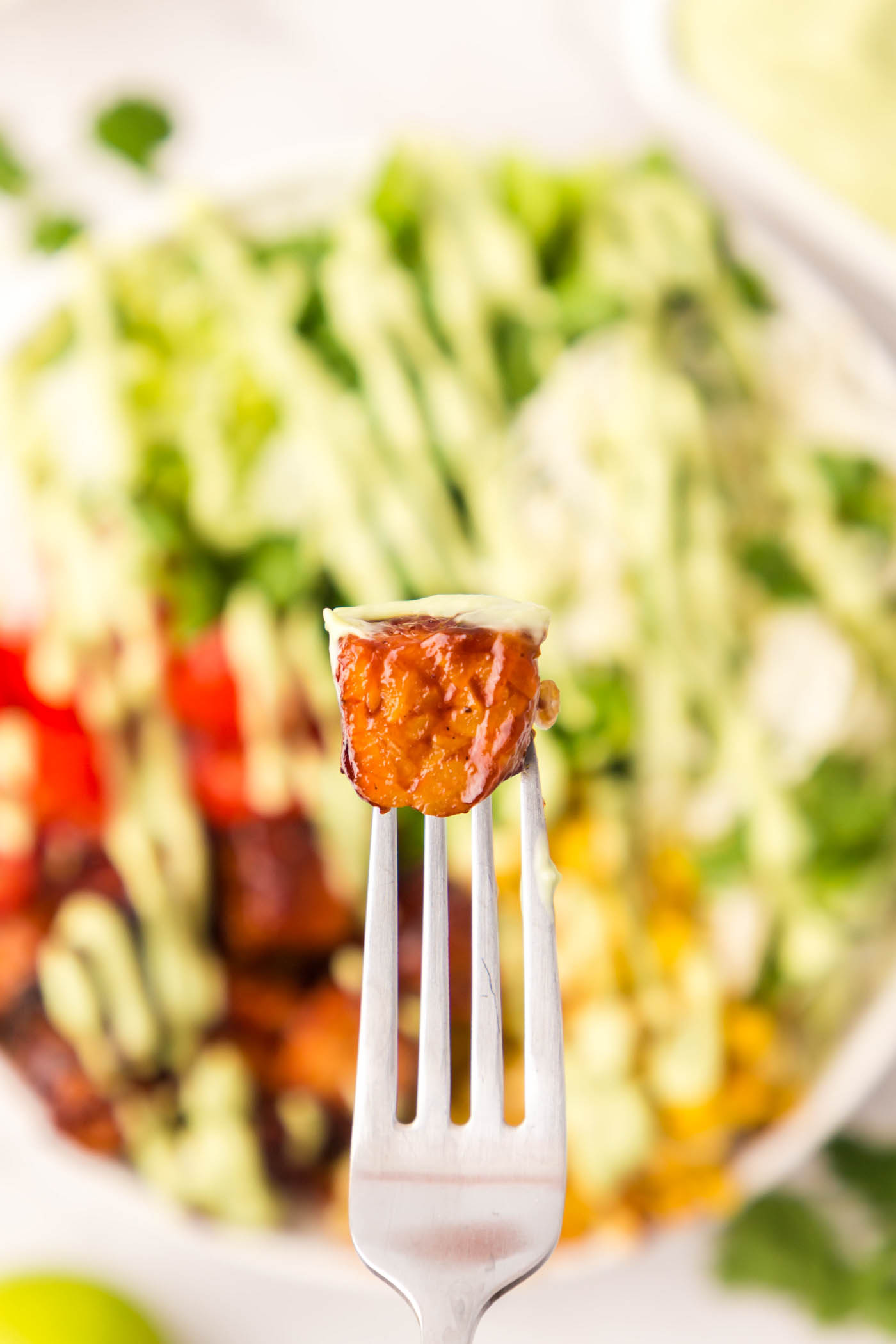 A cube of BBQ tempeh on a fork placed on top of the salad.