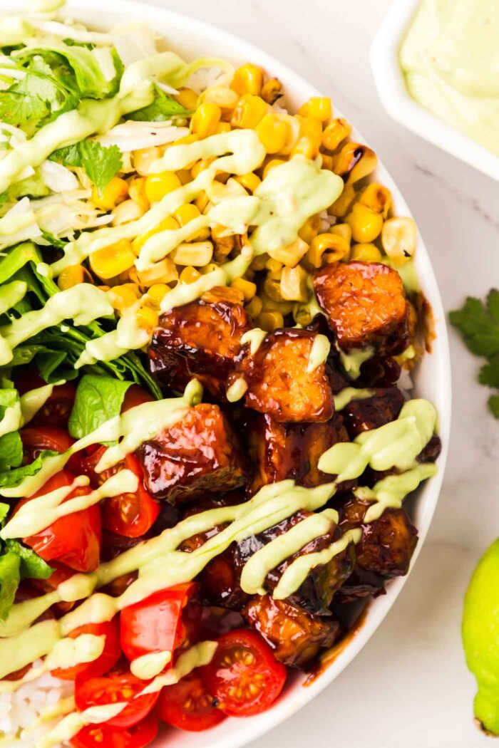 Close up overhead view of a BBQ tempeh bowl with tomato, corn, cabbage and a creamy avocado dressing.