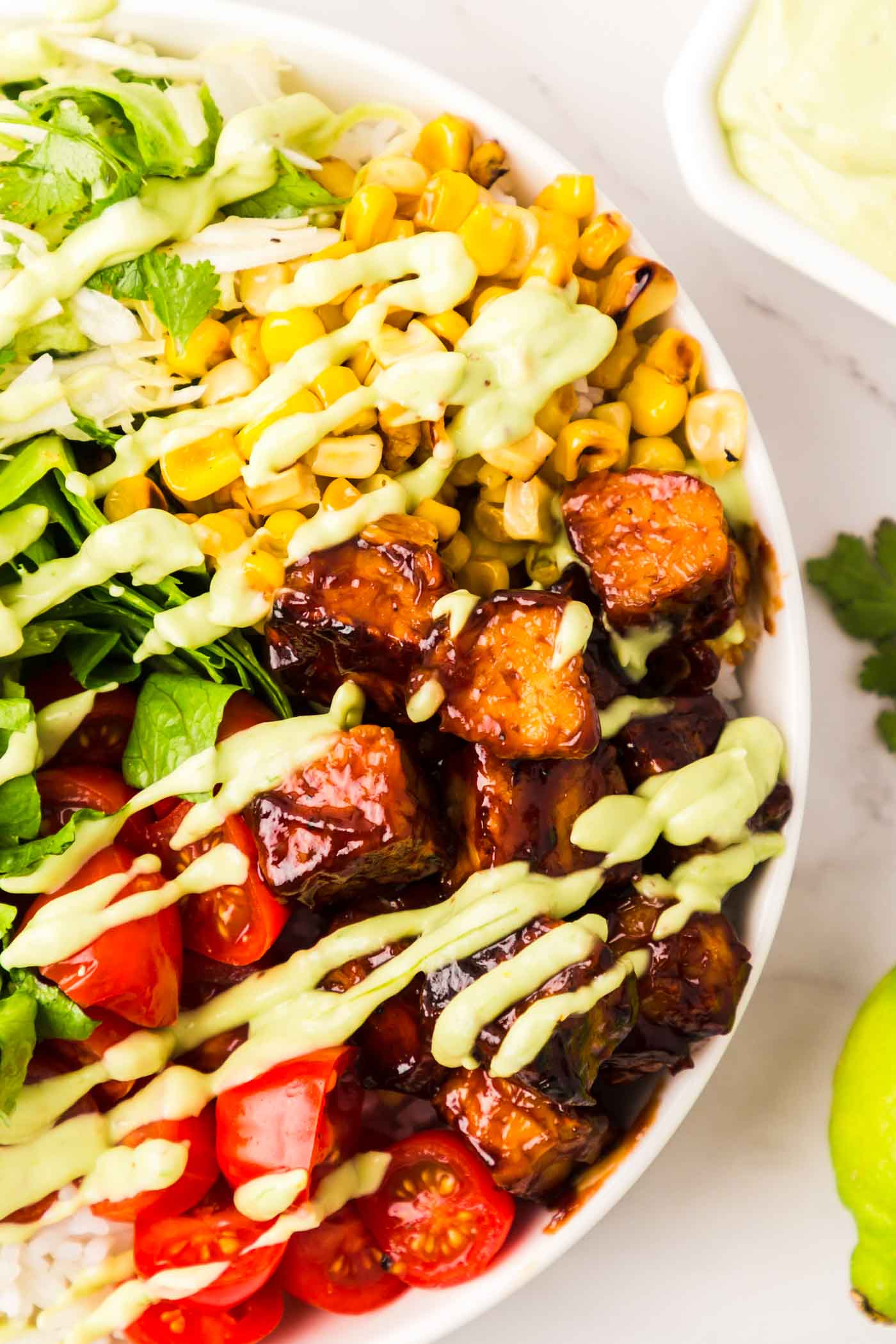 Close up overhead view of a BBQ tempeh bowl with tomatoes, corn, cabbage and a creamy avocado dressing.