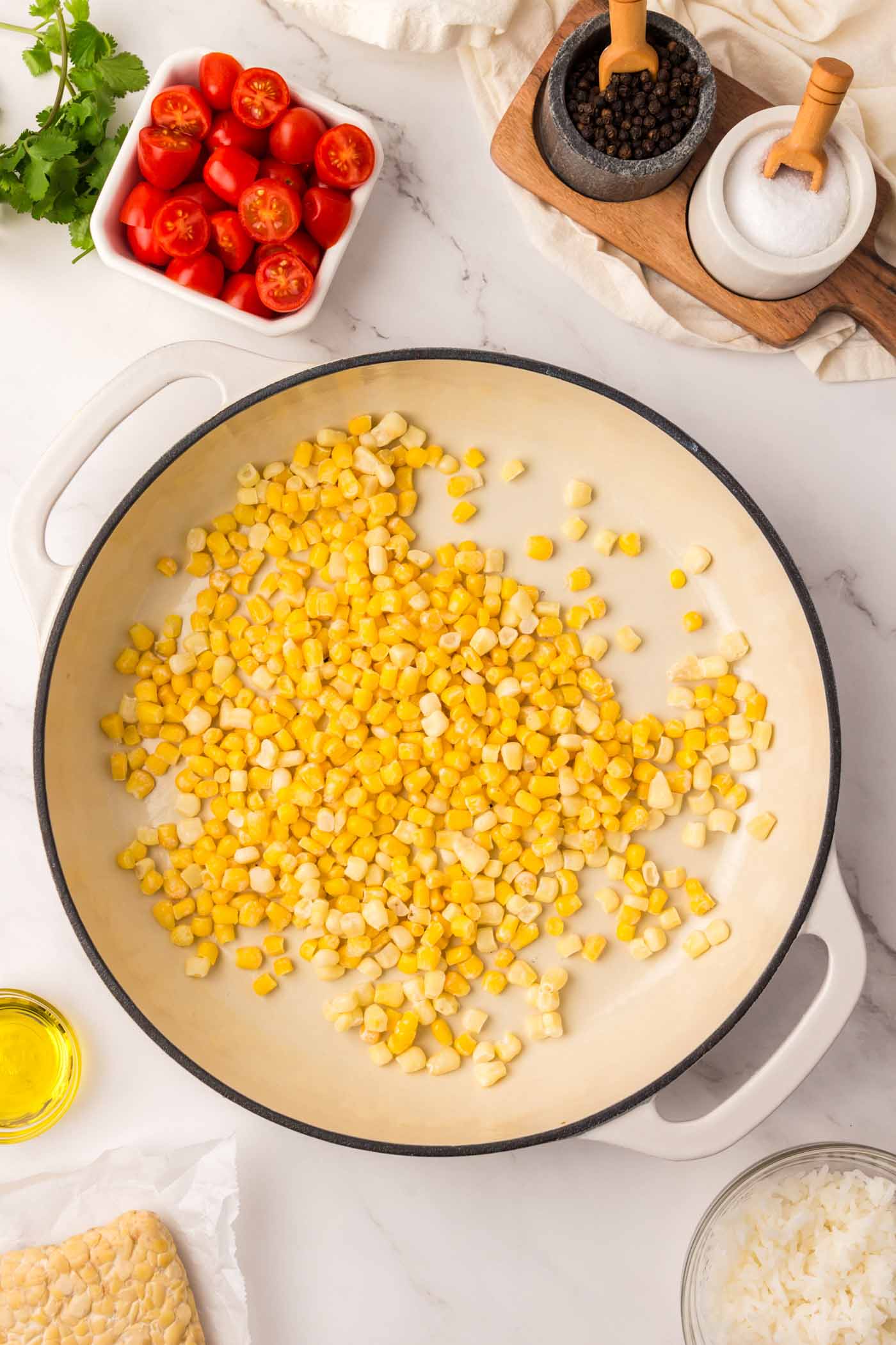 Corn kernels are cooking in a large pot next to a pot of tomatoes.