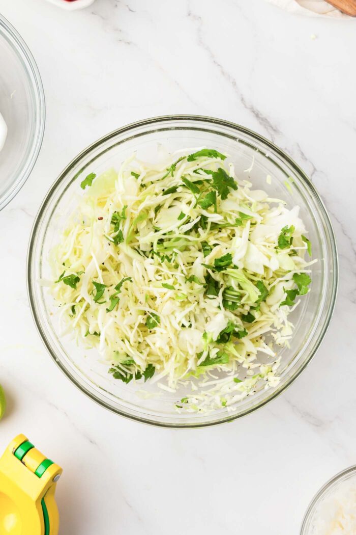 Shredded cabbage mixed with cilantro in a glass mixing bowl.