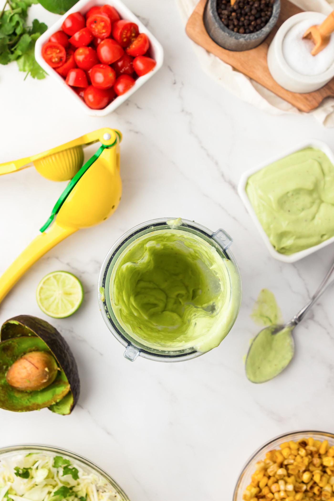 Bowl of dressing and a small blender jar of green dressing next to a citrus press.