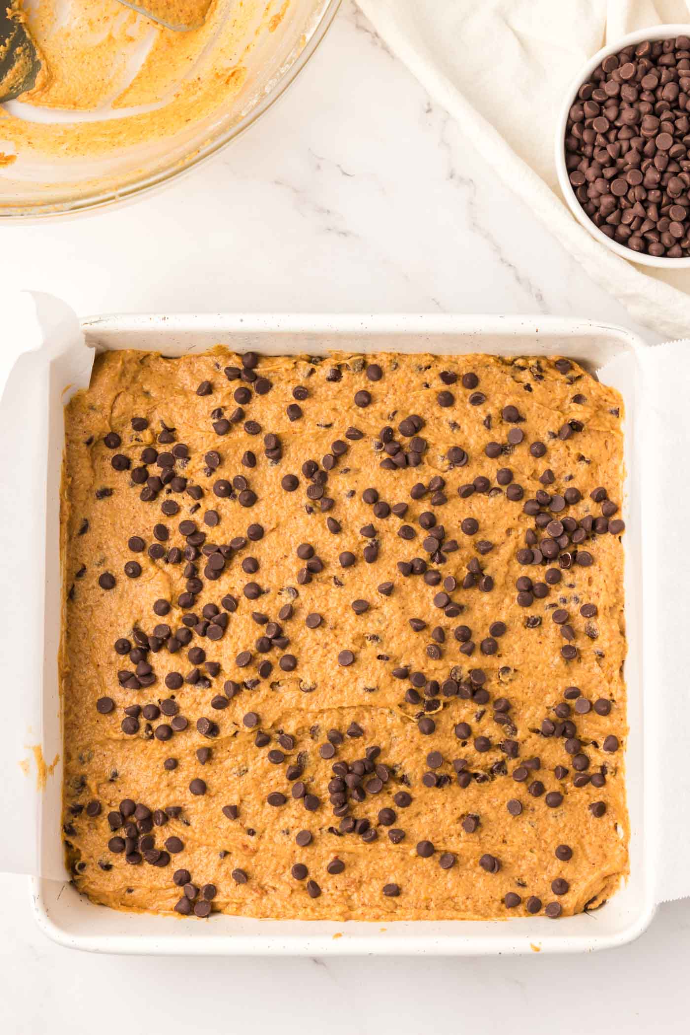 Unbaked pumpkin chocolate chip bars in a baking pan lined with parchment paper.