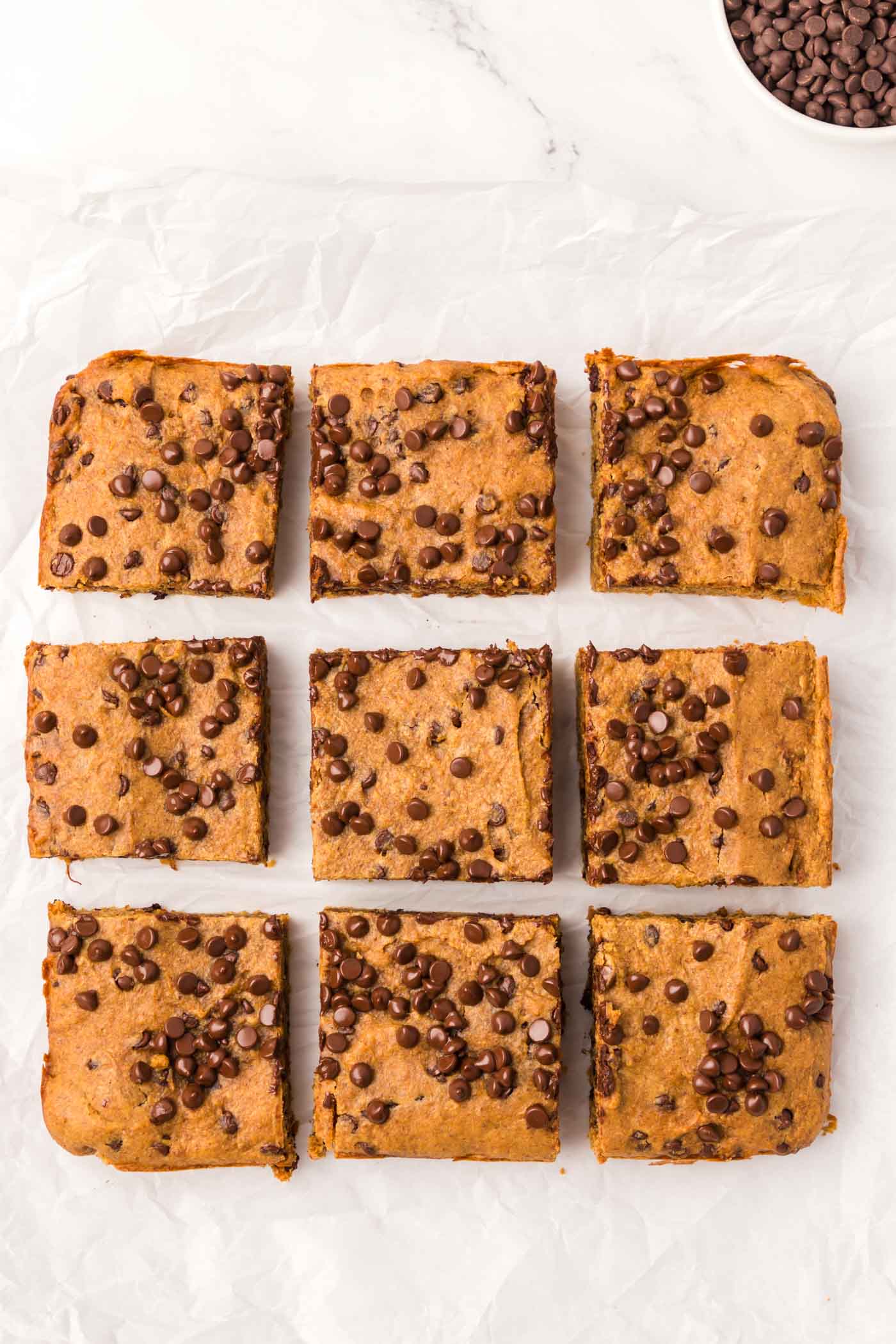 Baked pumpkin pie chocolate chip bars cut into 9 squares on a piece of parchment.