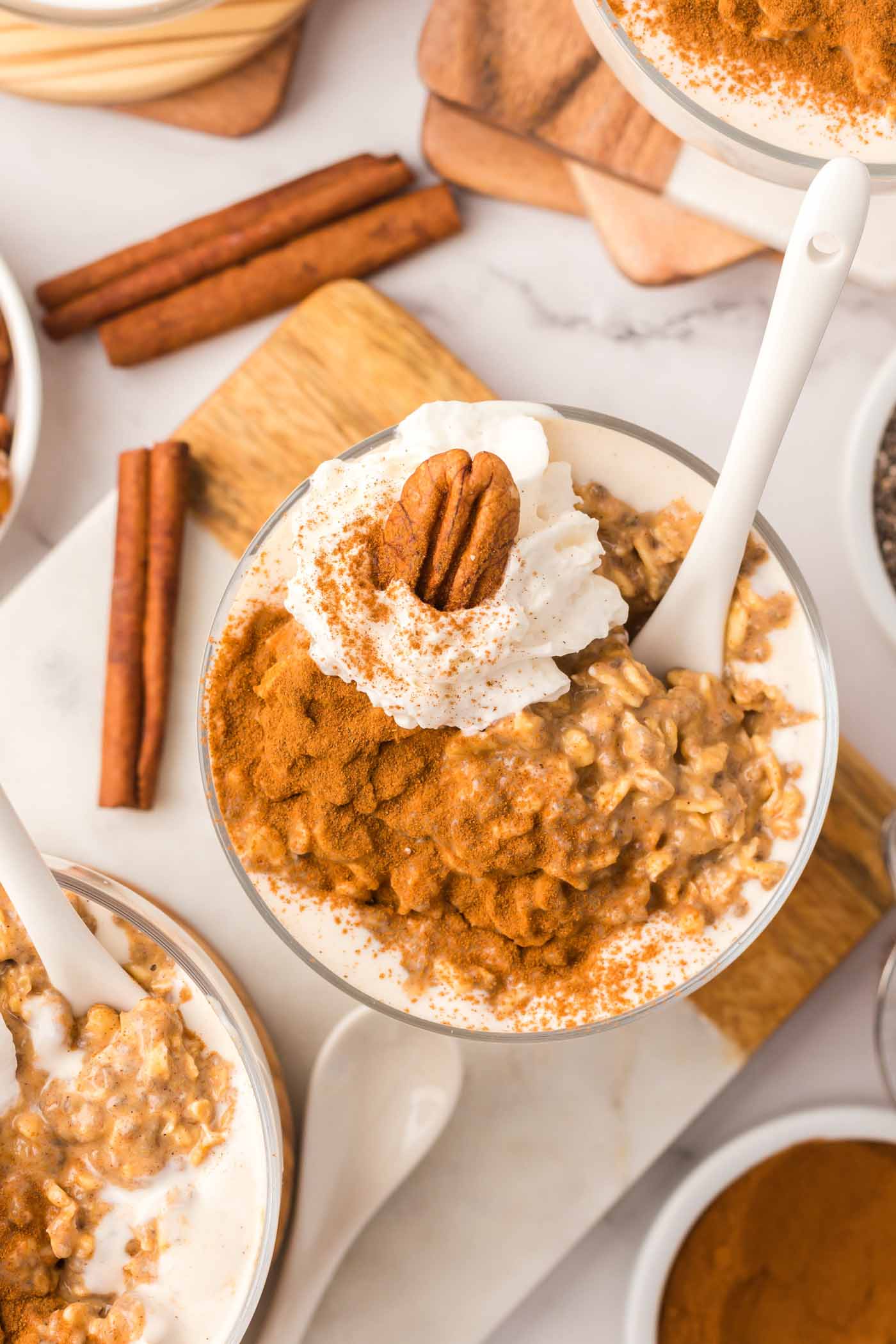 Overhead view of a parfait glass of pumpkin overnight oats topped with whipped cream a pecan and cinnamon.