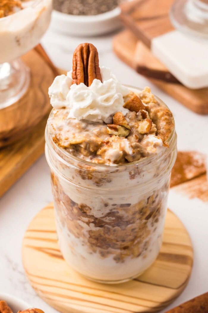 A jar of pumpkin overnight oats mixed with yogurt and topped with pecans and whipped cream.