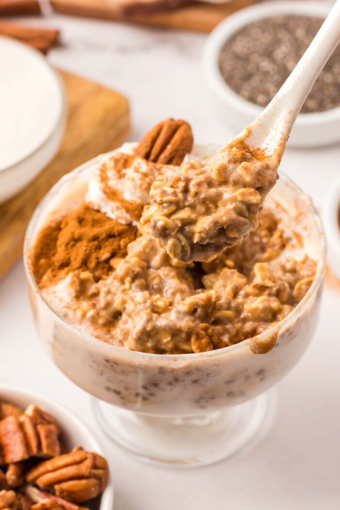 A spoon scooping pumpkin overnight oats from a bowl. The oats are topped with cinnamon and a pecan.