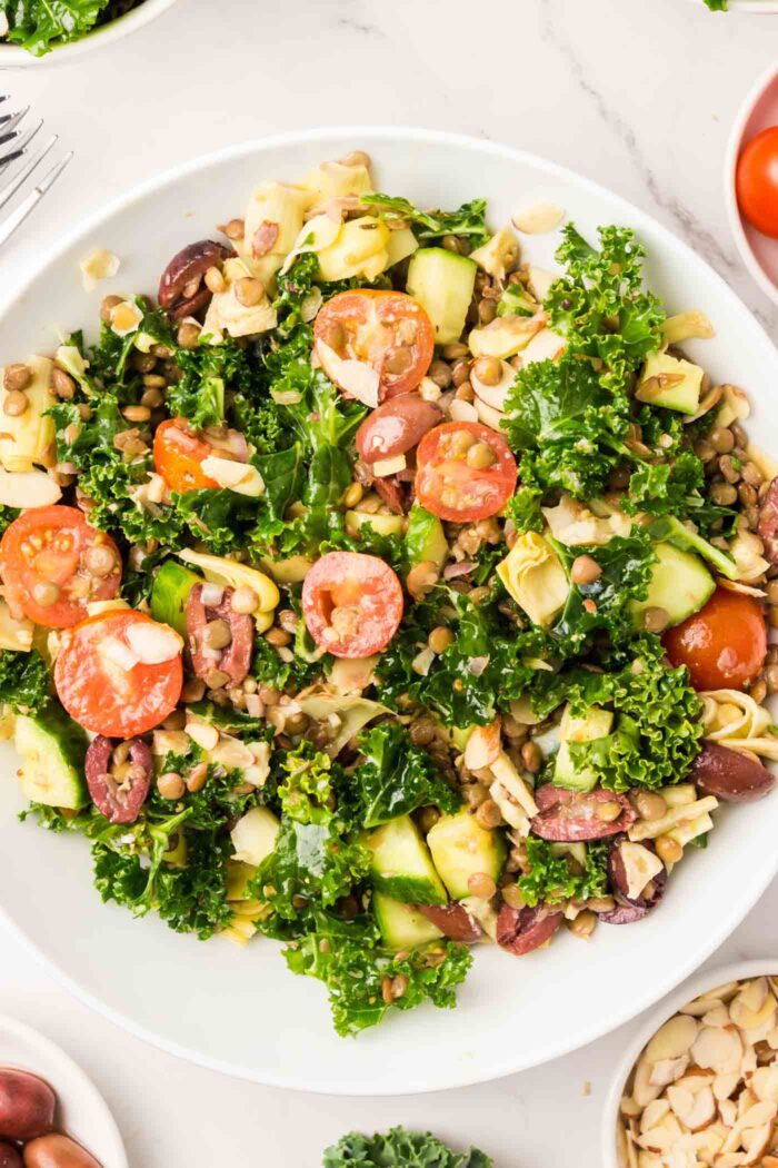 A lentil kale salad with tomato, almonds, cucumber and artichoke hearts in a bowl.