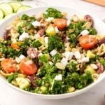 A large bowl of a kale salad with lentils, cucumber, feta, tomato and olives.