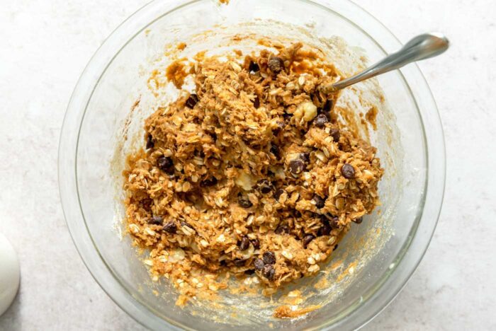 Thick peanut butter oatmeal chocolate chip cookie dough in a glass mixing bowl with a spoon.