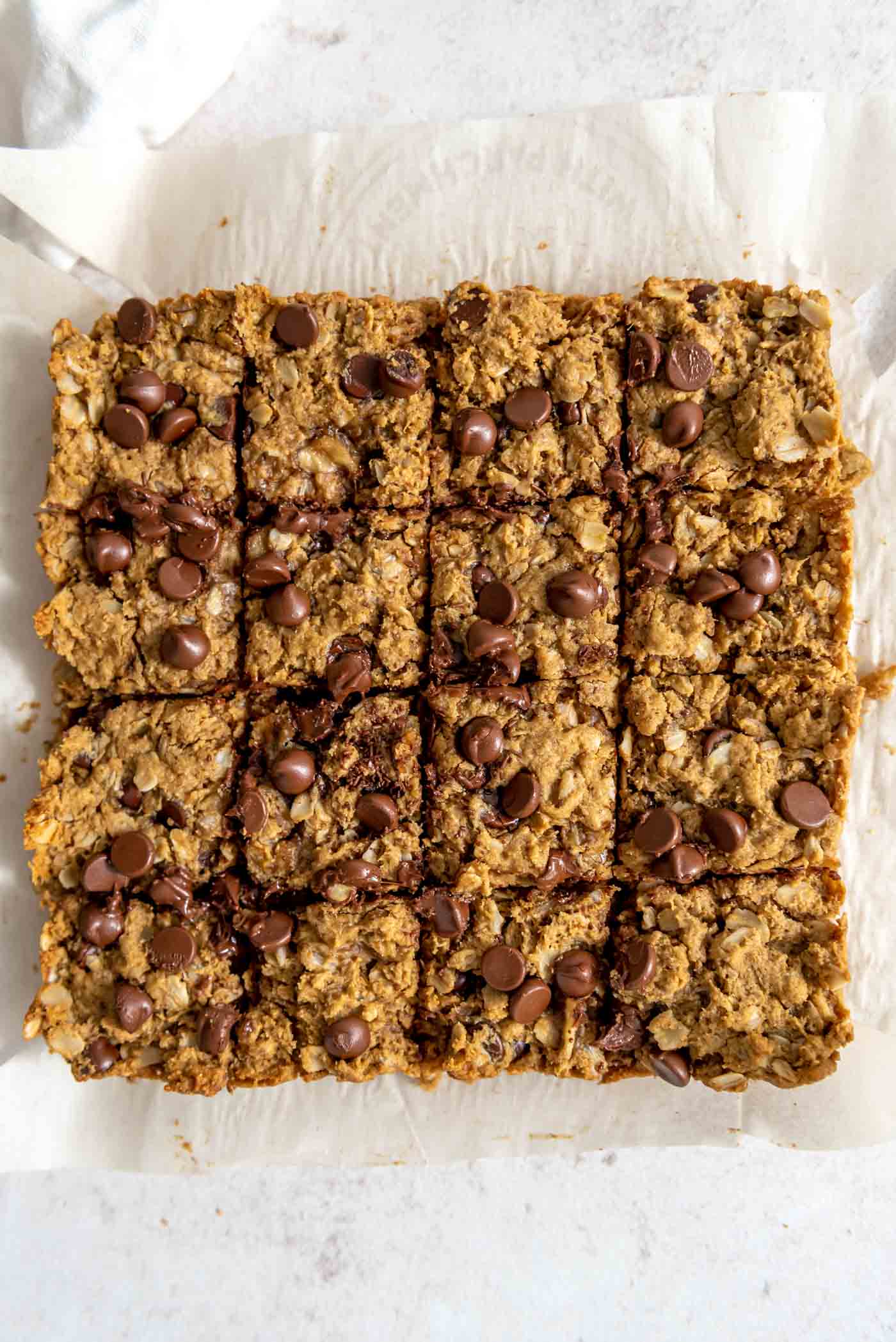 Overhead view of a batch of oatmeal chocolate chip cookie bars cut into 16 squares on a piece of parchment paper.