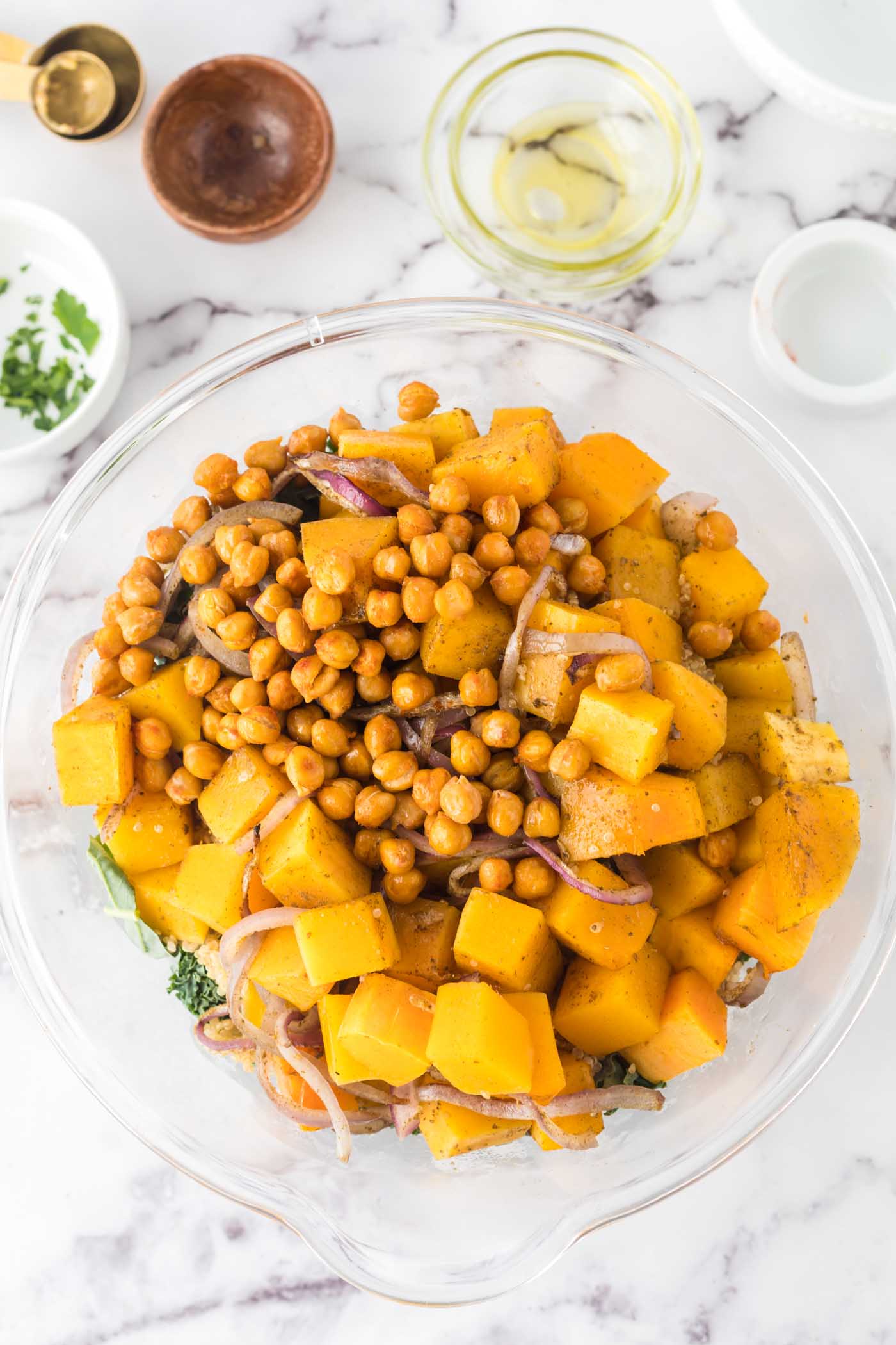 Roasted cubes of butternut squash in a mixing bowl with chocolate chips and red onion.