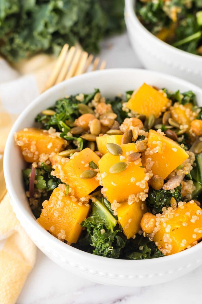 A bowl of butternut squash quinoa salad with kale, chickpeas and red onion in it.