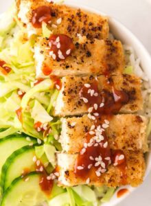 Close up of tofu katsu slices in a bowl with cabbage and cucumber.