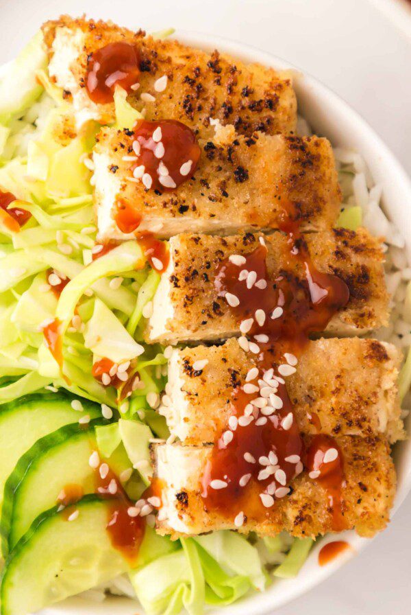 Close up of tofu katsu slices in a bowl with cabbage and cucumber.