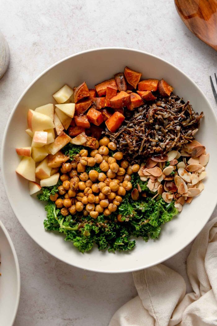 Overhead view of a harvest bowl with kale, chickpeas, apple, almonds and wild rice.