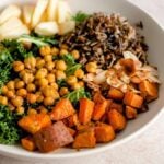 A bowl with roasted sweet potato cubes, chickpeas, apple, wild rice, slivered almonds and kale.