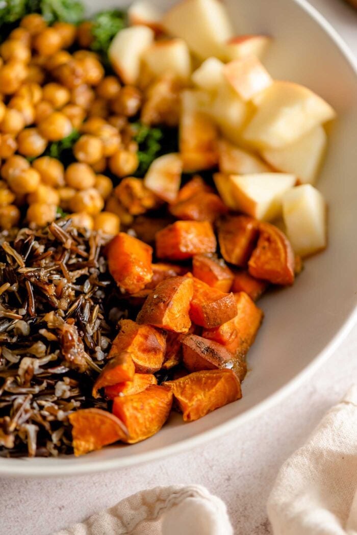Close up of roasted sweet potato in a bowl with kale, chickpeas and apple.