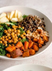 A bowl with roasted sweet potato cubes, chickpeas, apple, wild rice, slivered almonds and kale.