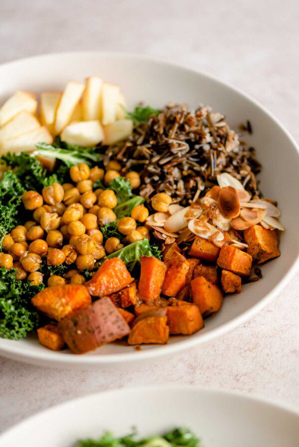 A bowl with roasted sweet potato cubes, chickpeas, apple, wild rice, slivered almonds and kale.