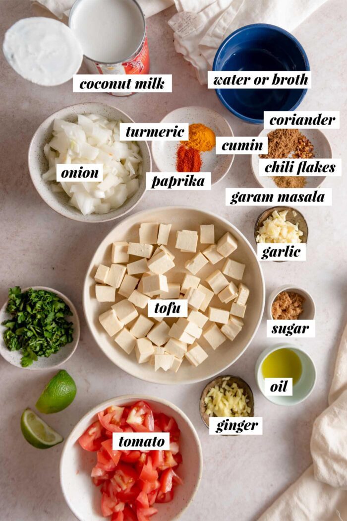 All the ingredients needed for making a vegan tofu coconut curry recipe with tomato, spices, onion and garlic.