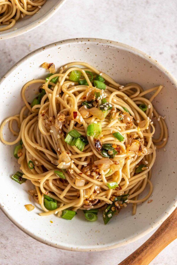 Overhead view of a bowl of garlic chili oil noodles topped with scallions and sesame seeds.