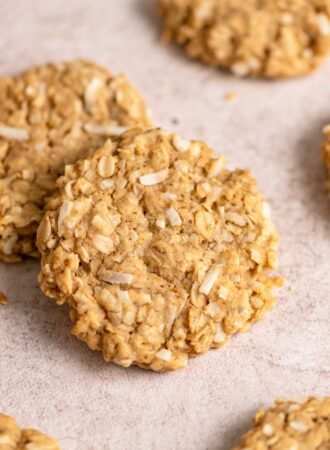 A coconut oatmeal cookie resting on another cookie with a few more cookies scattered around it.