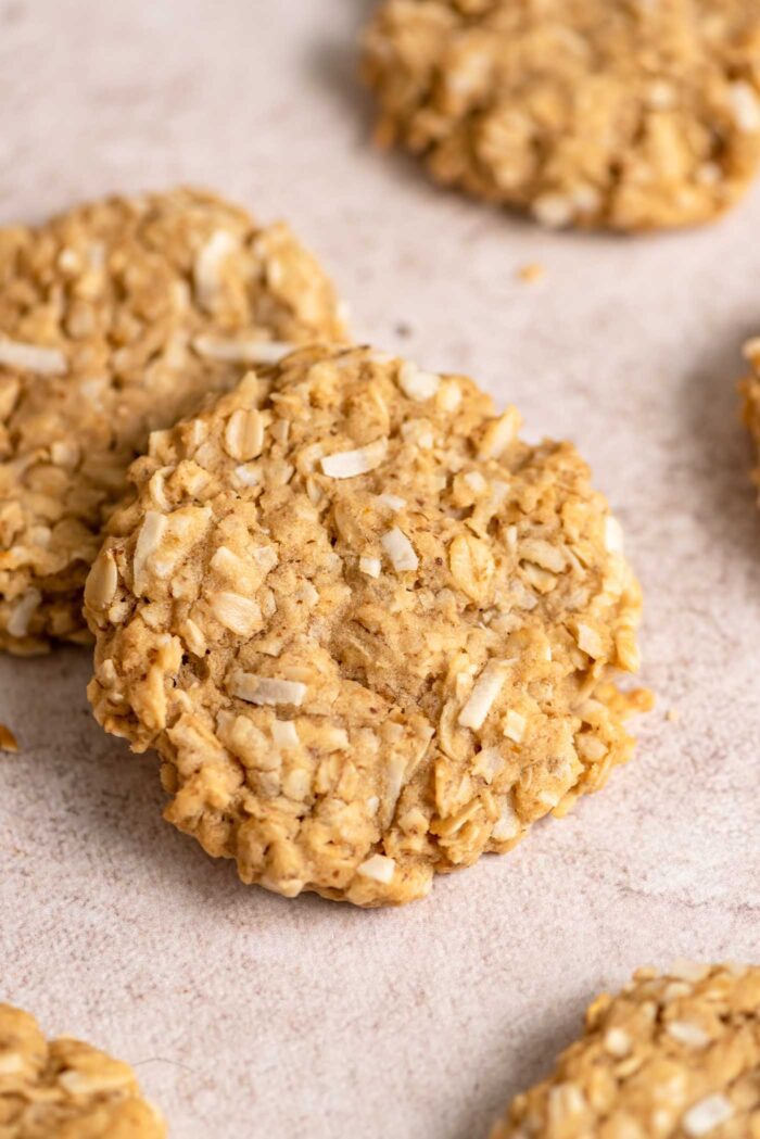 A coconut oatmeal cookie is resting on another cookie with several more cookies spread around it.