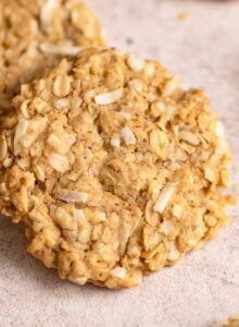 A coconut oatmeal cookie resting on another cookie with a few more cookies scattered around it.