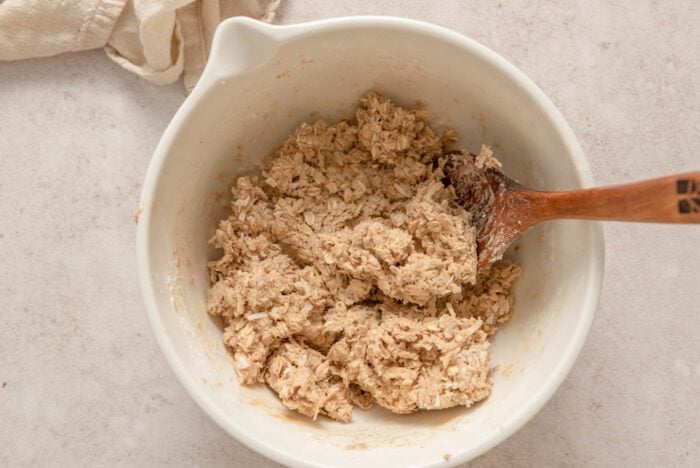 Coconut oatmeal cookie dough in a mixing bowl with a wooden spoon.