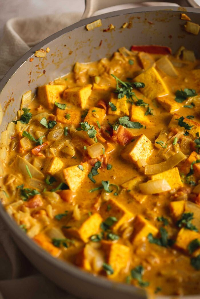 A creamy coconut curried tofu with diced tomato and onion topped with fresh cilantro cooking in a skillet.