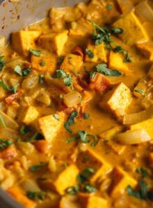 A creamy coconut curried tofu with diced tomato and onion topped with fresh cilantro cooking in a skillet.