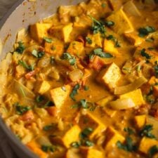 A creamy coconut curried tofu with diced tomato and onion topped with fresh cilantro cooking in a skillet.