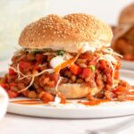 A sloppy joe on a plate. The sloppy joe filling is made from lentils and topped with a cabbage slaw.