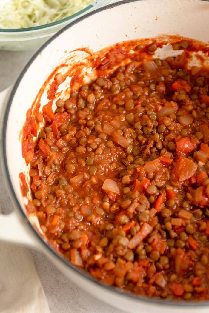 Lentils in a thick tomato sauce with diced onion and bell pepper cooking in a large pot.