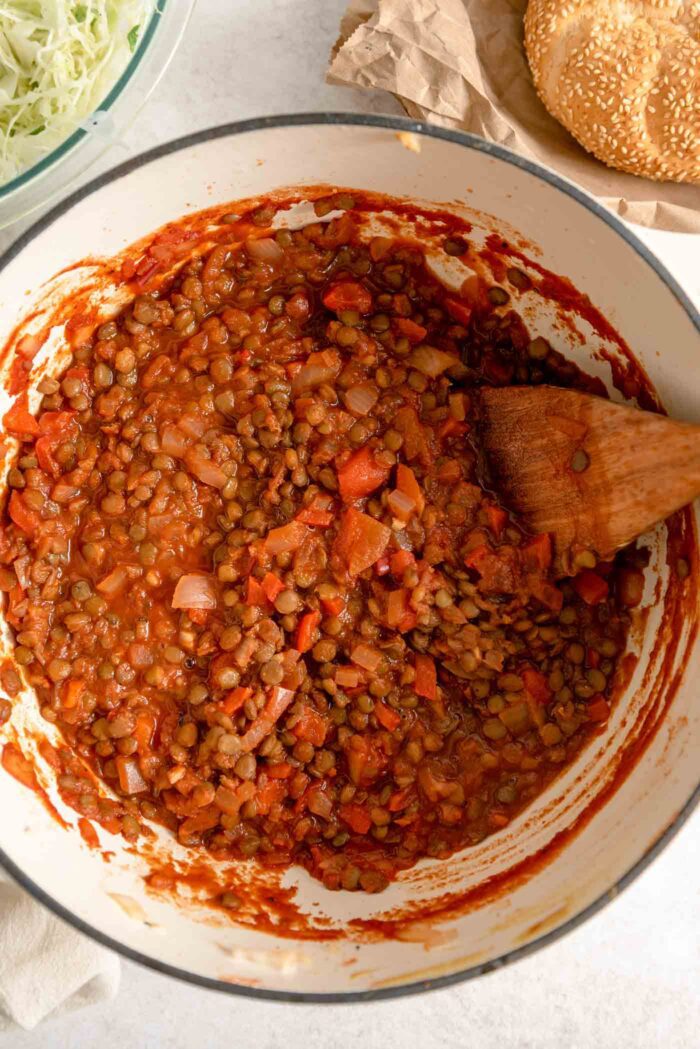 Vegan lentil sloppy joe sauce in a large saucepan with a wooden spoon.