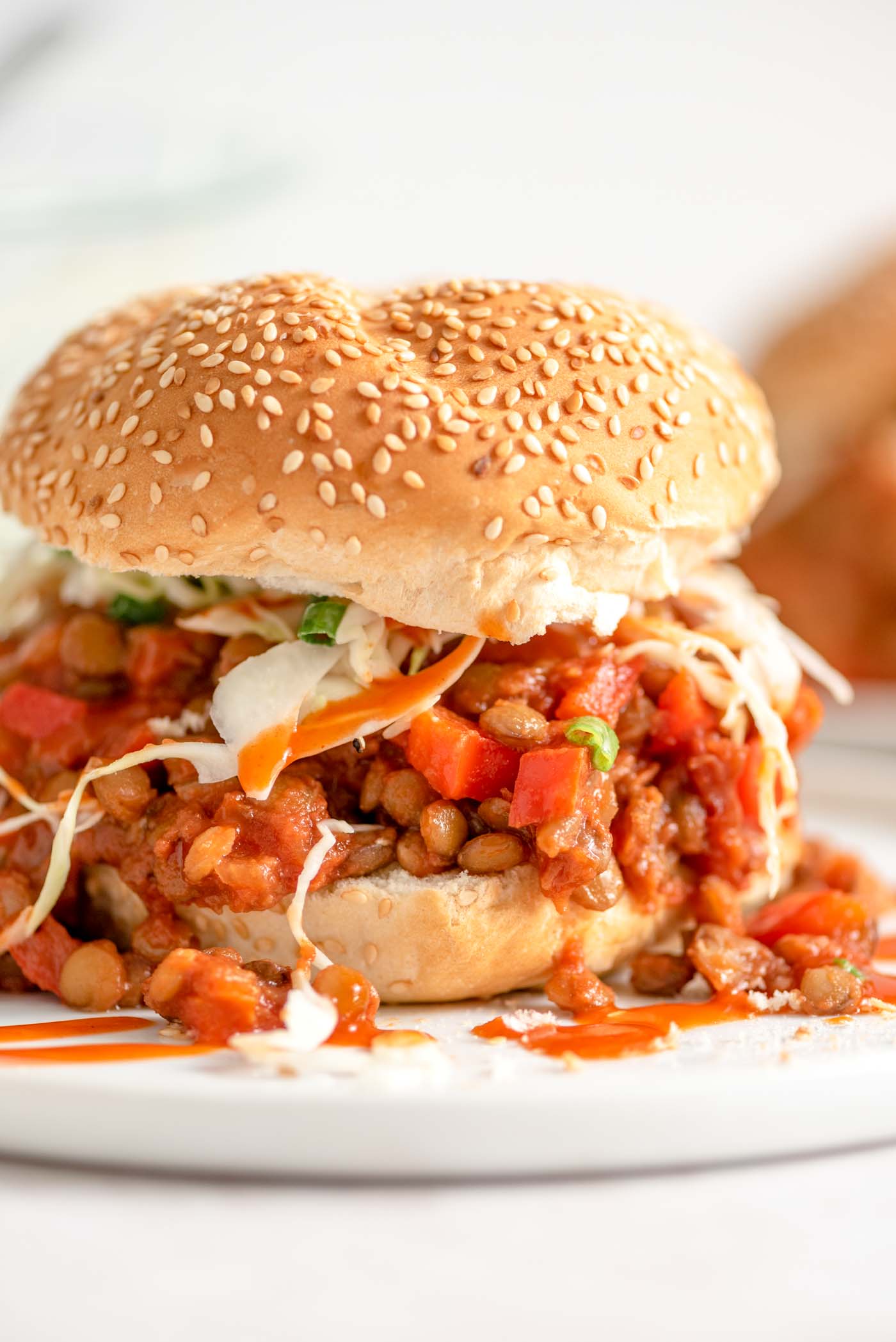 A lentil vegan sloppy joe sandwich with cabbage slaw drizzled with hot sauce on a plate.