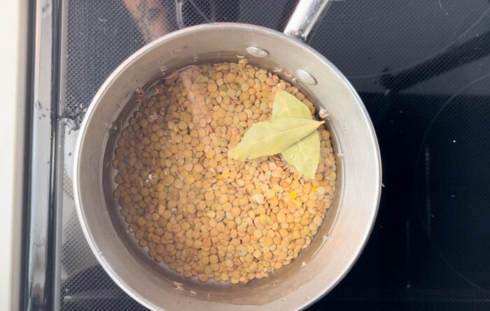 Green lentils cooking in a pot with a bay leaf in it.