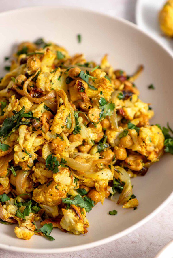 Curry roasted cauliflower salad with chickpeas, cashews, red onion and cilantro in a bowl.