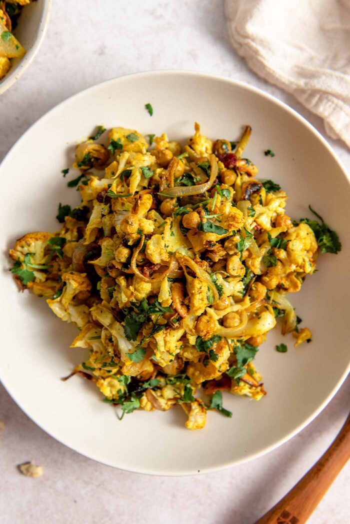 Overhead view of a colourful curry roasted cauliflower salad with cilantro, red onion, chickpeas and cranberries.