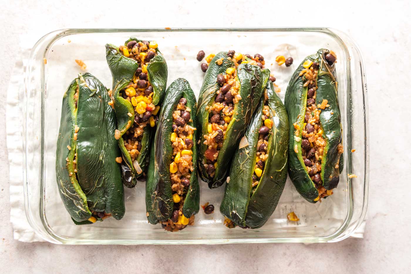 6 stuffed poblano peppers in a glass baking dish.