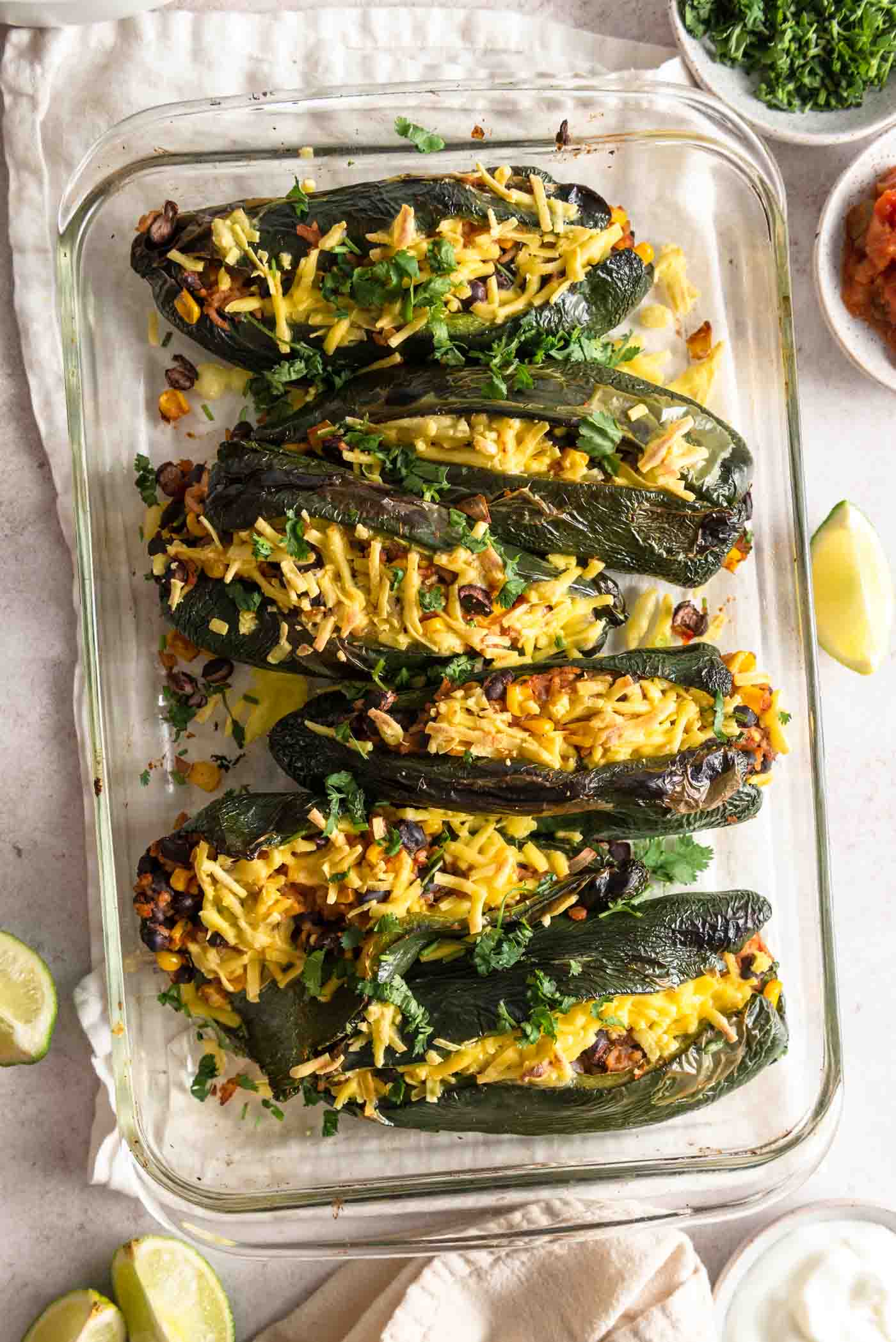 6 stuffed poblano peppers topped with shredded cheese in a baking dish.