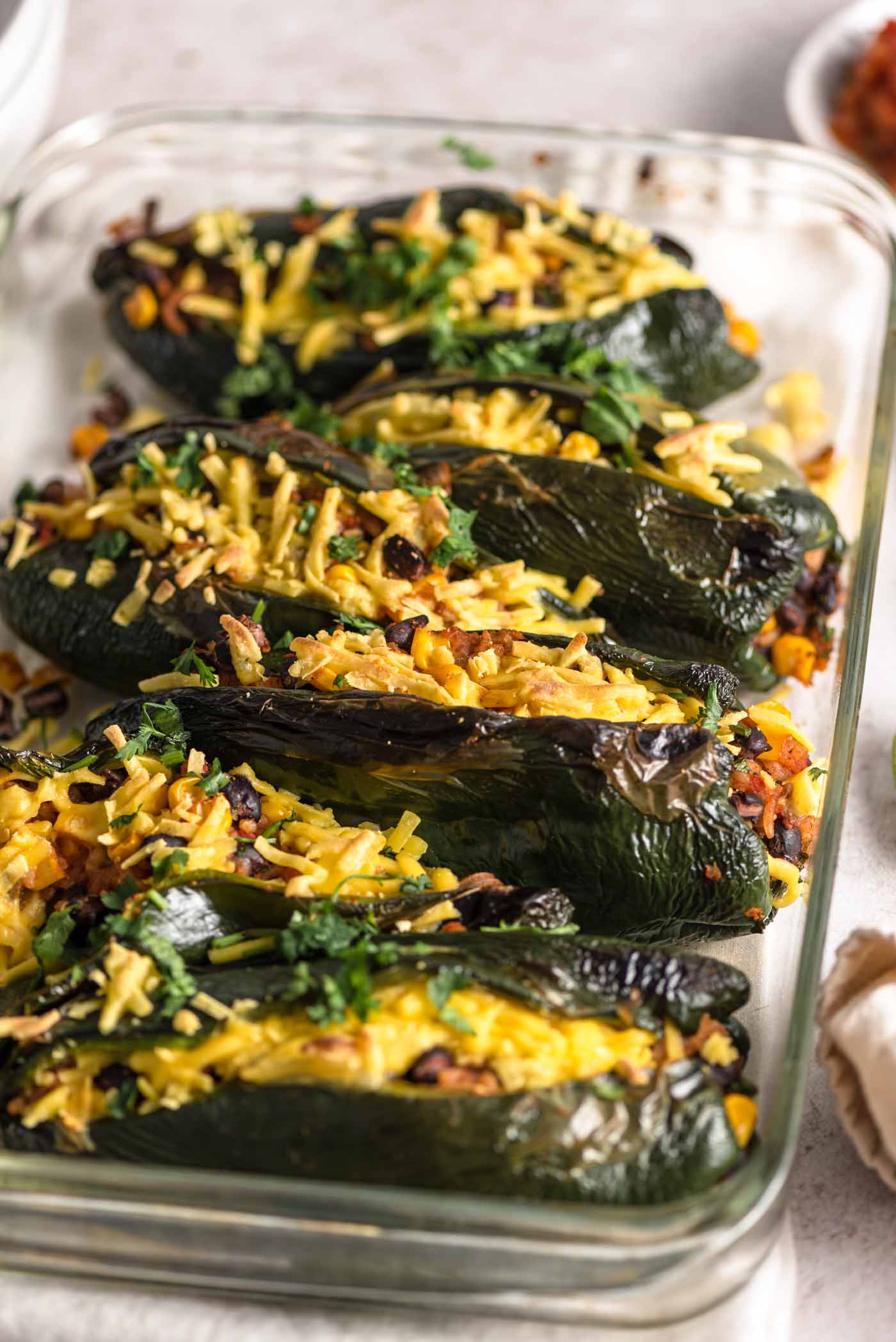 6 stuffed poblano peppers topped with cheese in a glass baking dish.