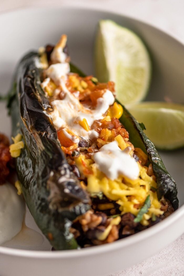 Close up of a vegetarian stuffed poblano pepper stuffed with a rice and bean mixture and topped with salsa and sour cream.
