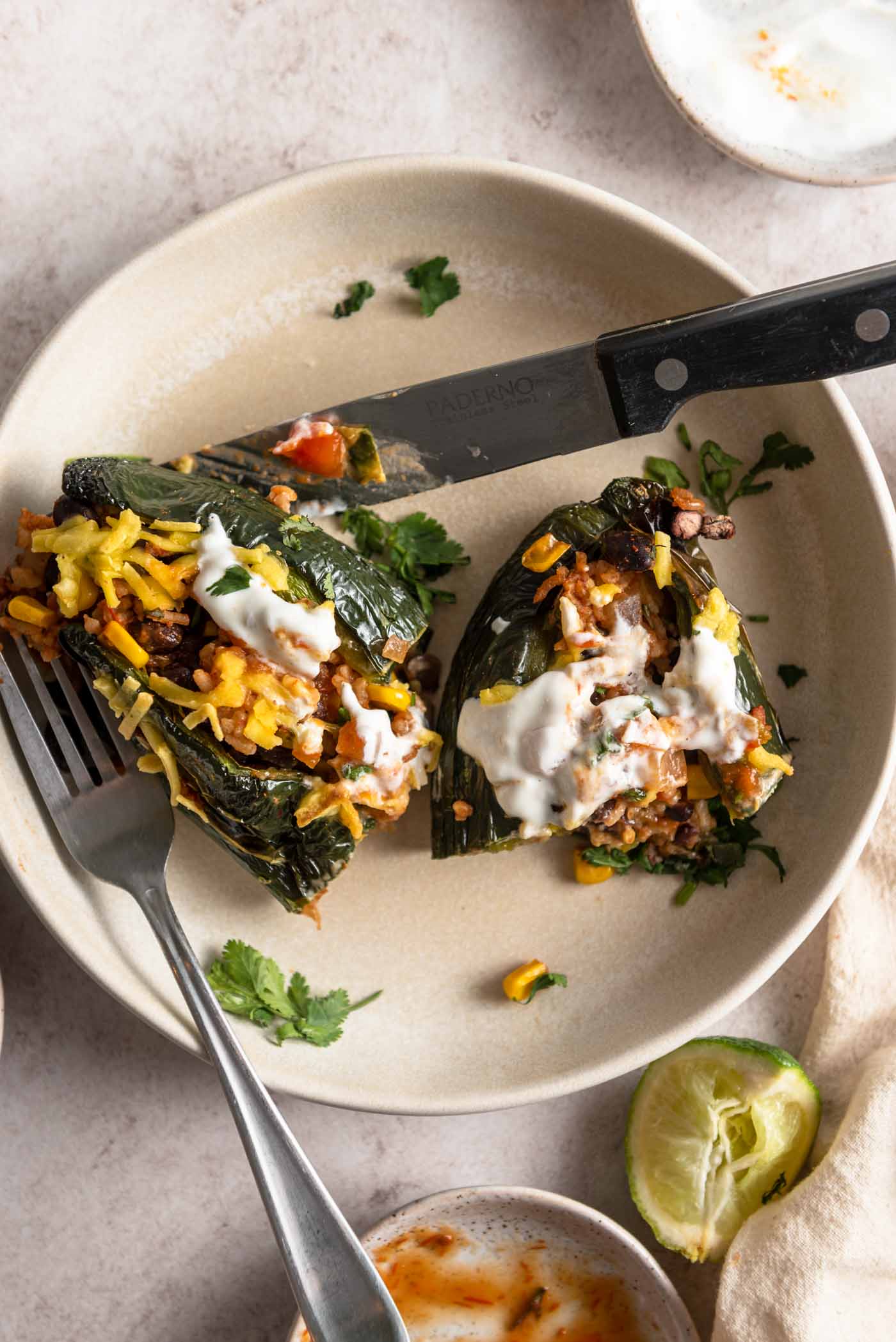 Overhead view of a stuffed poblano pepper topped with cheese and sour cream cut in half in a bowl.