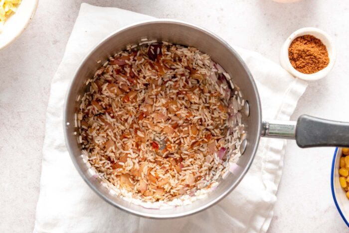 Rice mixed with red onion, garlic and spices in a small saucepan.